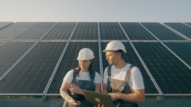 一位女工程师和一位穿着制服的工人正在检查太阳能电池板 他们正在做一个节能工程 工人们聚精会神地讨论系统的有效性 — 图库视频影像