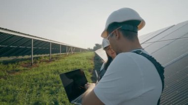 Bir dizüstü bilgisayar ve güneş panelleri yakınında çalışan bir mühendis modern elektrik teknolojilerini tartışıyor ve analiz ediyor. Yeşil elektrik kavramı. Yüksek kalite 4K görüntü.
