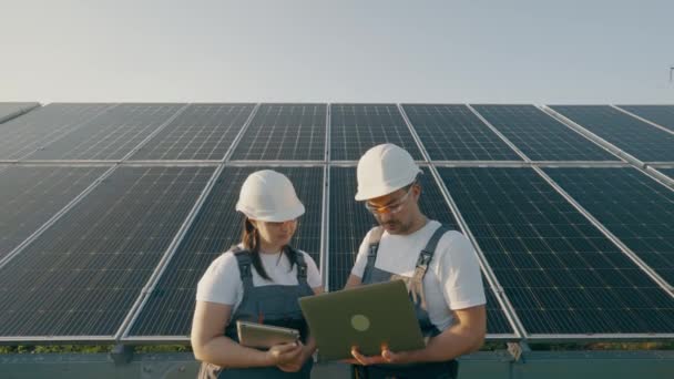 ソーラーパネルの動作を確認しながら 安全ヘルメットやベストで有能なエンジニアのリアビュー 男女共通のグリーンエネルギープロジェクトで協力しています — ストック動画