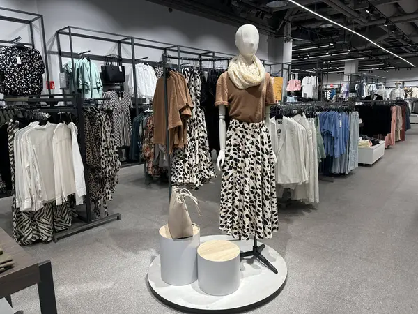 Varşova, Polonya - 28 Nisan 2025: Kahverengi bluz ve leopar desenli etek giyen şık manken, güncel moda eğilimlerini ve canlı atmosferi vurgulayan çeşitli giyim ürünleriyle dolu modern bir perakende mağazasında belirgin bir şekilde sergileniyor