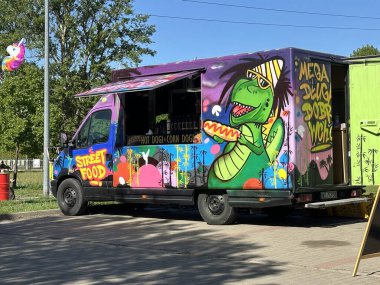 Varşova, Polonya - 04 Mayıs 2025 Dinazor duvar resmi içeren canlı bir yemek kamyonu, ağaçlarla dolu canlı bir açık havada lezzetli sokak yemekleri sunuyor.