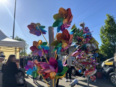 Varşova, Polonya - 04 Mayıs 2025: Canlı rüzgar fırıldakları, güneşli atmosferin keyfini çıkaran insanlarla birlikte açık hava pazarında sergilenmektedir.