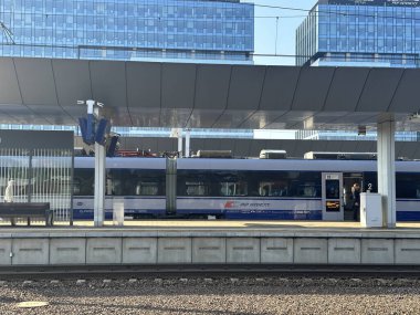 Modern tren, çağdaş mimari ve altyapı ile çevrili bir şehir platformunda, canlı bir ulaşım sahnesi yaratıyor.