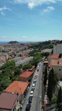Evleri ve caddeleri olan bir kıyı şehrinin havadan görünüşü. Sahne yeşil tepeler, mavi deniz ve açık bir gökyüzünü içeriyor. Turizm ve eğlence temaları için ideal.