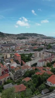 Konut binaları ve yeşillik karışımı bir kıyı şehrinin havadan görünüşü. Manzara arka planda tepeleri, açık mavi gökyüzünü barındırır. Sosyal medya içeriği, şehir markalaşması, turizm pazarlaması