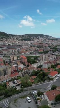 Konut binaları ve yeşillik karışımı bir kıyı şehrinin havadan görünüşü. Ufuk çizgisi açık mavi gökyüzünün altında bir tepe ve deniz zeminine sahiptir. Turizm içeriği, kentsel kalkınma projeleri