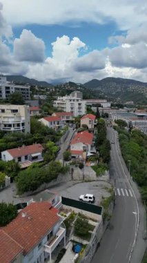Konut binaları, virajlı yollar ve arka planda yeşil tepeler olan kıyı kasabasının havadan görünüşü. Gökyüzü parçalı bulutlu, sakin bir atmosfer yaratıyor. Gayrimenkul, seyahat promosyonları