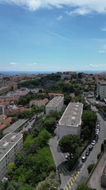 Yeşil tepeler ve konut binalarıyla çevrili dolambaçlı yolu olan bir şehrin havadan görünüşü. Gökyüzü parçalı bulutludur, manzaralı bir manzara yaratır..