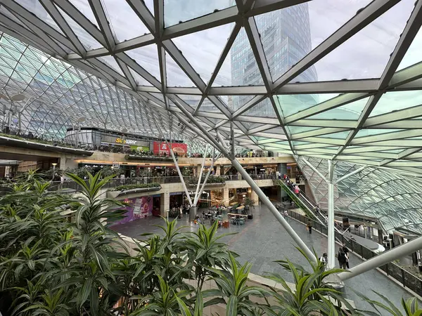 Varşova, Polonya - 22 Mayıs 2025: Cam çatı ve yemyeşil bitkilerin yer aldığı çağdaş bir alışveriş merkezinin iç görünümü, perakende alanları ve tasarım elementleri