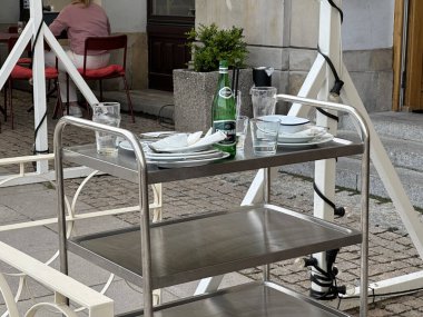 Varşova, Polonya - 22 Mayıs 2025: Paslanmaz çelik araba açık hava kafe ortamında, köpüklü su şişesi de dahil olmak üzere tabak ve bardaklar sergiliyor