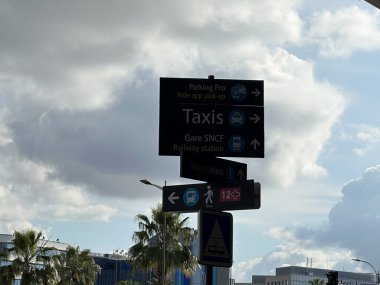 Taksi ve diğer hizmetleri gösteren bir tabela. Arka planda palmiye ağaçları ve bulutlu bir gökyüzü var.