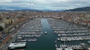 Park etmiş tekneleri ve arka planda bir şehri olan bir marinanın havadan çekilmiş videosu. Seyahat reklamları, kentsel yaşam tarzı içeriği, deniz veya kıyı teması, deniz kenarındaki tatil beldeleri için tanıtım videoları