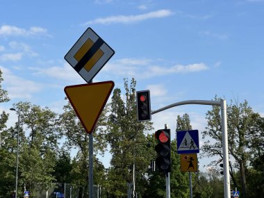 Varşova, Polonya - 22 Mayıs 2025: Trafik işaretleri yol koşullarını ve yaya uyarılarını gösteriyor, arka planda kırmızı ışıklar ve yemyeşil alanlar var