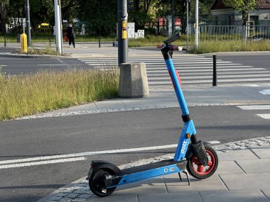 Varşova, Polonya - 22 Mayıs 2025: Elektrik scooter 'ı yaya geçidinin yanında duruyor, parlak mavi rengini ve yakınındaki çimlerle şehir merkezini vurguluyor.