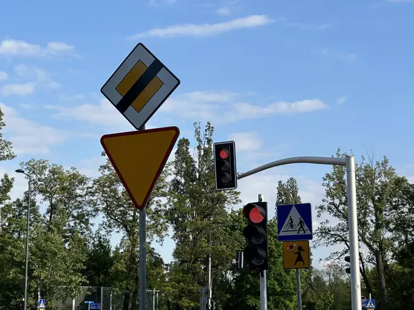 Varşova, Polonya - 22 Mayıs 2025: Trafik işaretleri yol koşullarını ve yaya uyarılarını gösteriyor, arka planda kırmızı ışıklar ve yemyeşil alanlar var