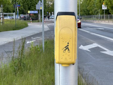 Varşova, Polonya - 22 Mayıs 2025: Sarı yaya sinyal düğmesi direğin üzerine monte edilmiş, kentsel alanda yeşil yakındaki inşaat çalışmalarının sinyalini veriyor