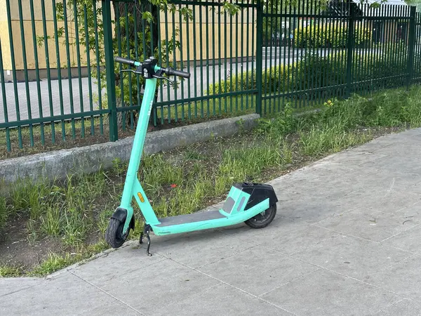 Varşova, Polonya - 22 Mayıs 2025: Elektrikli scooter yeşil çitin yanındaki kaldırıma park edilmiş, kentsel hareketlilik ve sürdürülebilir ulaşım seçeneklerini vurguluyor
