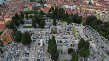 Büyük bir mezarlığın havadan görünüşü, şehir binaları. Sayısız mezar taşı ve patika, huzurlu bir dinlenme yeri. Hafıza, ölümlülük, zaman geçişi, araştırmacı gazetecilik, alışılmadık simgeler.