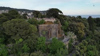 Nice 'teki Chateau Hill şelalesinin havadan çekilmiş videosu, yemyeşil alan, aşağıdaki şehir manzarası. Manzarası, doğal ve kentsel unsurlar. Seyahat reklamları, emlak sunumları, tatil blogları.