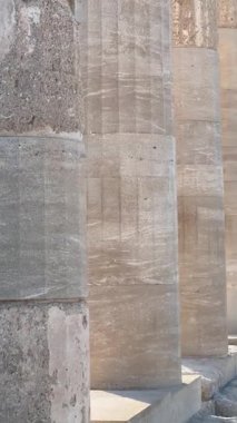 Taş sütunlar, sakin bir atmosfer ve berrak mavi gökyüzü ile çevrili ayrıntılı dokuları ve gölgeleri vurgulayan tarihi bir ortamda görkemli bir şekilde yükselir.