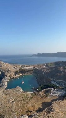 Kıyı manzarasında kayalık uçurumlar, berrak mavi sular ve yamaçtaki büyüleyici beyaz binalar, huzurlu ve resimsel bir manzara yaratıyor.