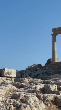 Tarihsel taş sütunlar parlak mavi gökyüzüne karşı kayalıklarda görkemli bir şekilde dururlar. Antik mimariyi ve doğanın güzelliğini sakin bir ortamda vurgularlar.