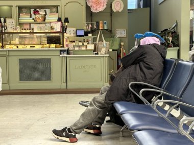 Güzel, Fransa - 10 Mayıs 2025: Havalimanı sandalyelerinde rahat bir şekilde uyuyan yorgun bir gezgin. Sahne, hava yolculuklarında yaygın olarak görülen yorgunluk, gecikme veya uzun konaklamaları yakalar.