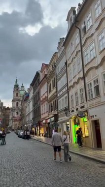 Prag, Çek Cumhuriyeti - 23 Nisan 2023: Prag 'da renkli mimari ve St. Nicholas Kilisesi ile tarihi sokak sahnesi, canlı bir kentsel atmosfer yarattı