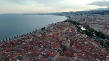 Sahilde canlı çatılar, dolambaçlı sokaklar ve arka planda dağlar olan sakin bir sahil manzarası kentsel manzarayı ve doğal güzelliği gösteriyor.