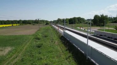 Tren yolu, parlak mavi gökyüzünün altında canlı yeşil tarlalar ve ağaçlar boyunca uzanıyor. Doğadaki yolculuklar ve maceralar için huzurlu bir ortam sunuyor.