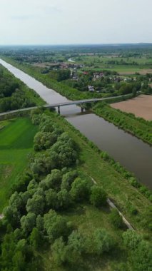 Bereketli yeşil tarlalar ve ağaçlarla çevrili dolambaçlı bir nehrin havadan görünüşü. Bir köprü nehri geçiyor, manzaranın iki tarafını birleştiriyor..