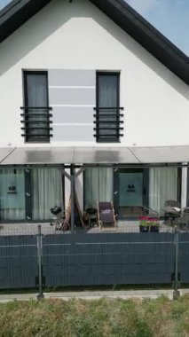 Terası olan modern bir ev. Ev beyaz bir cephe, büyük pencereler ve dış mobilyalarla kaplı bir verandaya sahip. Araziyi çit sarmış..