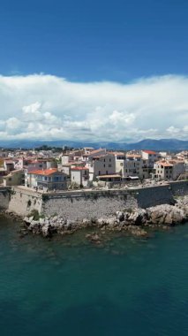 Turkuaz suların yanında tarihi bir taş kale, büyüleyici binalar ve dramatik bulutların oluşturduğu manzaralı kıyı manzarası sakin bir atmosfer yaratıyor.