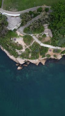 Hava perspektifi canlı yeşil ve dolambaçlı yollarla kayalık kıyı şeridini yakalıyor, sakin suları ve kıyı manzarasının güzelliğini vurguluyor.