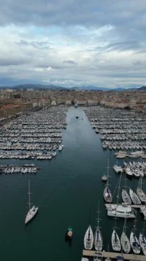 Canlı şehir binaları ve dramatik bulutlu gökyüzü tarafından çerçevelenmiş sayısız tekne ve yatın yer aldığı canlı bir marina sahnesi, kıyı yaşamının özünü yakalıyor.