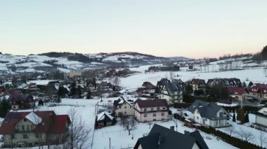 Karla kaplı bir kış köyünün manzaralı manzarasında ağaçlar ve tepelerle çevrili büyüleyici evler, huzurlu ve huzurlu bir ortam yaratıyor.