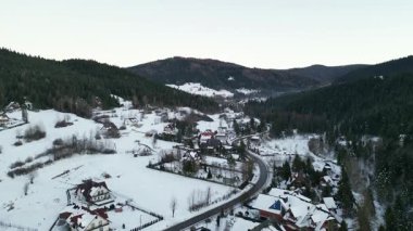 Karla kaplı evleri, yemyeşil ormanları ve dolambaçlı yolları olan sakin ve davetkar bir atmosfer yaratan kış harikalar diyarı manzarası.