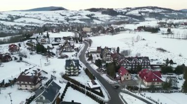Karla kaplı bir kış köyünün manzaralı perspektifi, rahat evler, dolambaçlı yollar, geniş beyaz manzaralar, sakin bir kış manzarası yaratıyor.