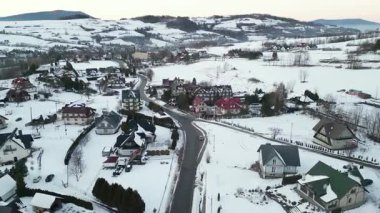 Karla kaplı bir kış köyünün manzaralı perspektifi, antika evler, dolambaçlı yollar ve sakin manzaralar, barışçıl bir atmosfer yaratıyor.