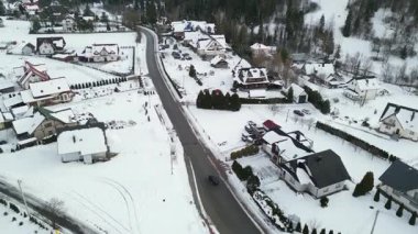 Yukardan çekilen karla kaplı yerleşim bölgelerinde evler, ağaçlar ve dolambaçlı yollar mevsimlik görüntüler için ideal sakin bir kış manzarası yaratıyor.