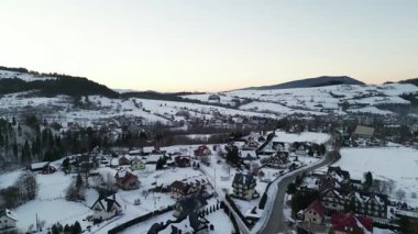 Karla kaplı bir kış köyünün manzaralı perspektifi, konforlu evler, dolambaçlı yollar ve huzurlu bir dağ zeminiyle, huzurlu bir atmosferi çağrıştırıyor.