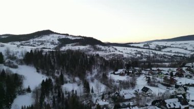 Karla kaplı manzarada ağaçlar ve tepelerle çevrili büyüleyici evler, manzaralı kırsal bir ortamda kışın dinginliğini yakalıyorlar.
