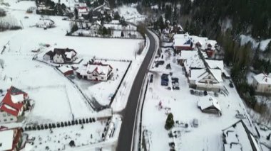 Karla kaplı evleri, kıvrımlı yolları ve yemyeşil ormanları olan, barışçıl ve davetkar bir atmosfer yaratan kış harikalar diyarı manzarası.