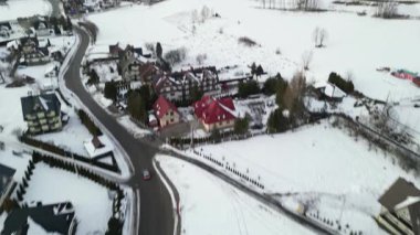 Manzaralı kış manzaraları kar örtülü tarlalar ve büyüleyici evler, arka planda yumuşak tepeler ve sakin bir pastel gökyüzü ile huzurlu bir atmosfer yaratıyor.