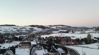 Vadide karla kaplı evler, arka planda kayan tepeler ve dağlar olan manzaralı bir kış köyü, sakin ve pitoresk bir atmosfer yaratıyor.