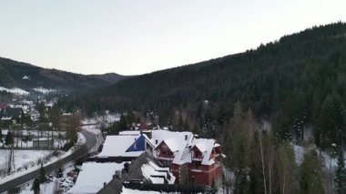 Konforlu ahşap kulübeler, karla kaplı çatılar, sakin bir kış manzarasıyla çevrili. Etrafı yeşil ağaçlar ve uzak dağlarla çevrili. Huzurlu bir geri çekilme ortamı yaratıyor.