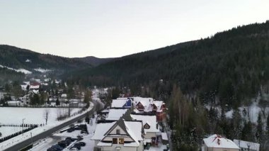 Kış manzaraları karla kaplı evleri gösteriyor. Etrafı yemyeşil ağaçlarla çevrili, dolambaçlı bir yol. Sakin dağ manzarasını kesiyor ve manzarayı aydınlatıyor.