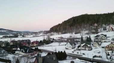 Karla kaplı tarlalar, büyüleyici evler, dolambaçlı yollar, kışın kırsal bir arazinin sükunetini yakalayan bir kış manzarasının çarpıcı hava perspektifi.