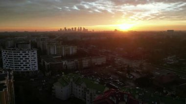 Gün batımında şehrin ufuk çizgisi, çeşitli binaları ve çatıları aydınlatıyor, altın ışık manzaranın üzerine sıcak bir ışık saçıyor, sükunet ve güzelliği çağrıştırıyor.