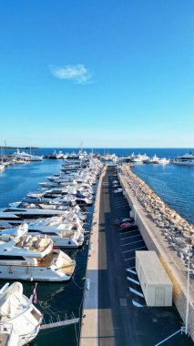Rıhtımda berrak gökyüzü ve sakin sularla hizalanmış lüks yatların yer aldığı liman sahnesi, huzurlu bir sahil atmosferini çağrıştırıyor.